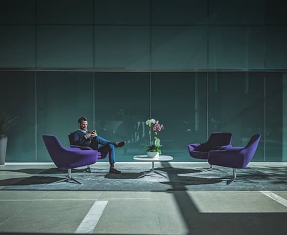 GAIOL Homem sentado em uma poltrona mexendo no celular.